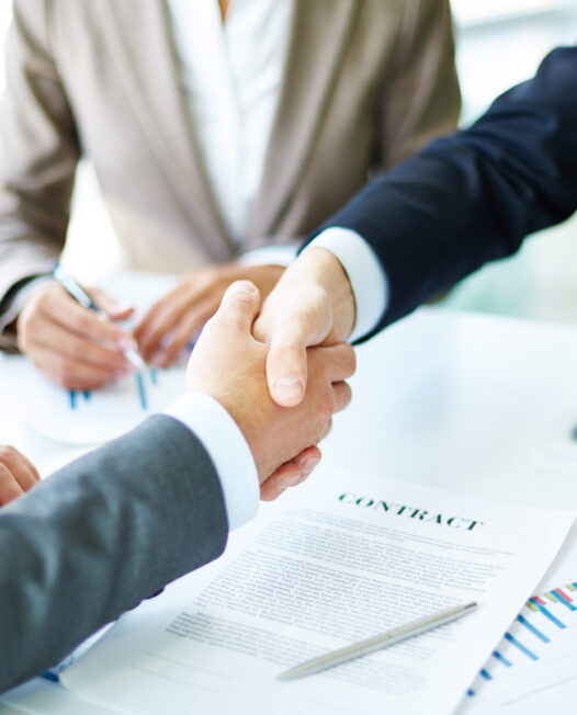 Image of business partners handshaking over business objects on workplace